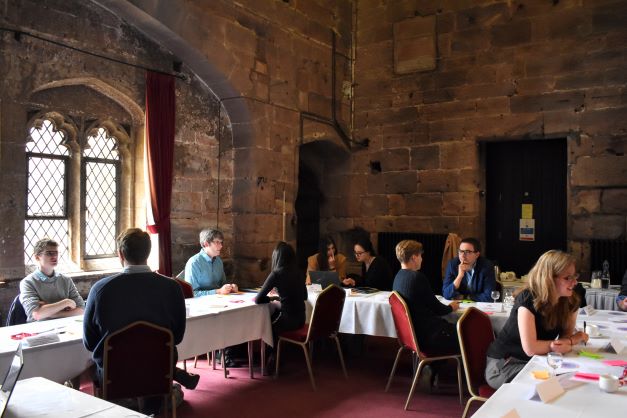 Data impact fellows promo image - people sat around tables in a stone walled room with leaded windows.