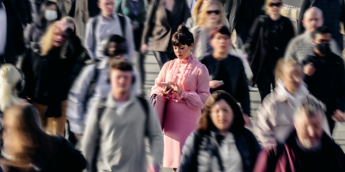 Elevated view of businesswoman dressed in pink standing on London Bridge and checking mobile device while crowd of people pass on their way to work. Used to illustrate the breadth of the UK Data Service Annual Report for 2022-23.