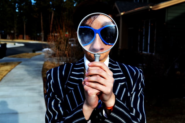 person in pinstripe jacket with magnifying glass in front of their face