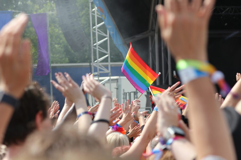 Crowd at Clifton Downs, Bristol. Rainbow flag held above waving hands. By Robin Worrall for Unsplash.